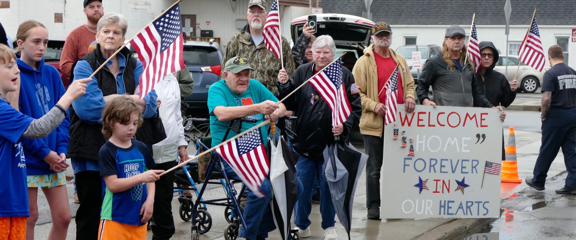 Homecoming crowd holding flags and a sign while waiting for the Veterans to return.